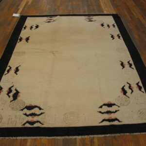 Large cream rug with a black border and repeating pink and black abstract motifs on wood plank flooring.