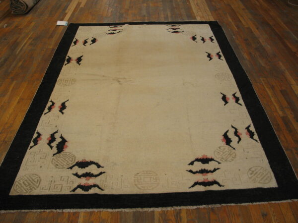 Large cream rug with a black border and repeating pink and black abstract motifs on wood plank flooring.