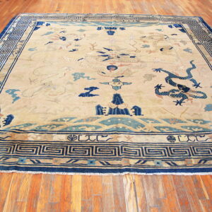Tan rug with blue dragon patterns and geometric borders laying on shiny reddish-brown hardwood.
