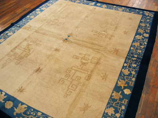 Low-pile beige rug with subtle geometric patterns and a bright blue floral border on a brown wood floor.