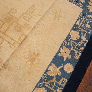 Beige rug with a faded geometric center and blue floral border lies on reddish-brown hardwood flooring.