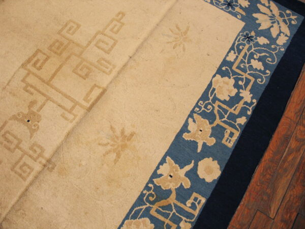 Beige rug with a faded geometric center and blue floral border lies on reddish-brown hardwood flooring.