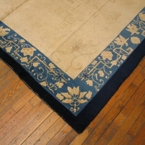 Tan rug corner showing blue floral borders and a navy edge, placed on distressed wood planks.