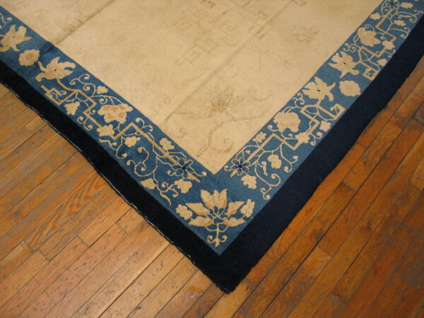 Tan rug corner showing blue floral borders and a navy edge, placed on distressed wood planks.