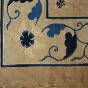 Detail of a tan rug featuring carved floral and vine designs in light beige and deep blue.