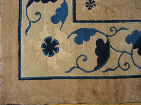 Detail of a tan rug featuring carved floral and vine designs in light beige and deep blue.
