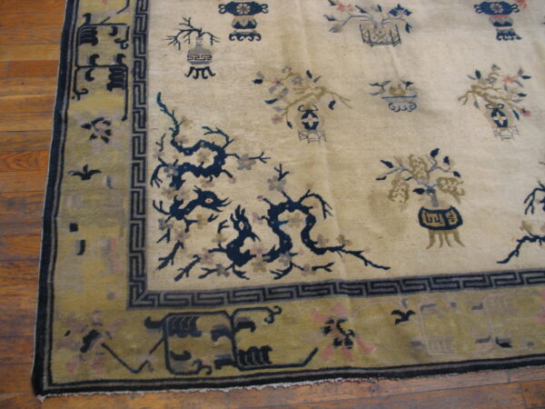 Cream rug with scattered blue and taupe vase motifs and dragons, framed by an olive green border on wood planks.