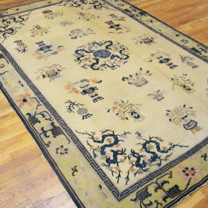 Pale yellow rug featuring dark blue and pink scattered traditional motifs, a medallion, and bordered by wood floors.