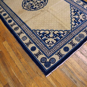 Beige rug with a navy blue border featuring Greek key patterns and cultural symbols on wood planks.
