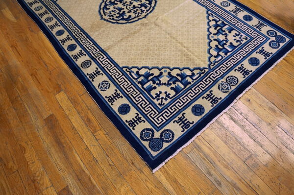 Beige rug with a navy blue border featuring greek key patterns and cultural symbols on wood planks.