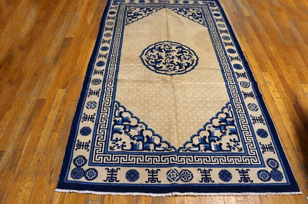 Low-pile rug in tan and deep blue featuring geometric and medallion designs on glossy wood flooring.