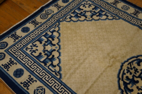 Tan rug with complex blue greek key and symbol borders lying on warm brown wood flooring.
