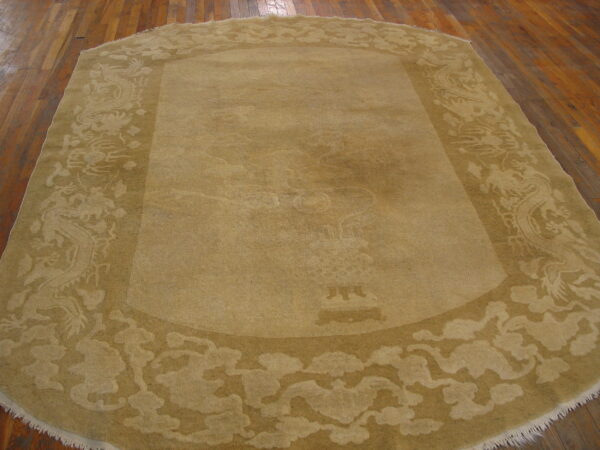Rounded rectangular tan rug with a sculpted border featuring dragons and clouds over wood planks.