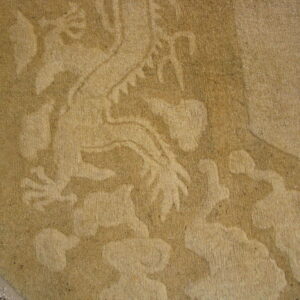 Tan tone-on-tone rug with a carved mythical design rests on dark reddish-brown floorboards.