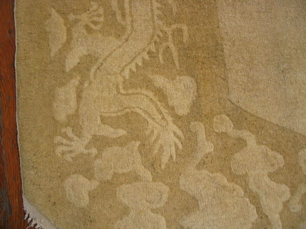 Tan tone-on-tone rug with a carved mythical design rests on dark reddish-brown floorboards.