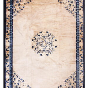 A light beige rug with a blue floral medallion and corner spandrels, framed by a wide navy border.