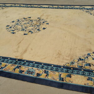 Large beige rug with navy and teal borders featuring a floral medallion on a concrete floor.