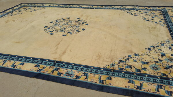 Large beige rug with navy and teal borders featuring a floral medallion on a concrete floor.