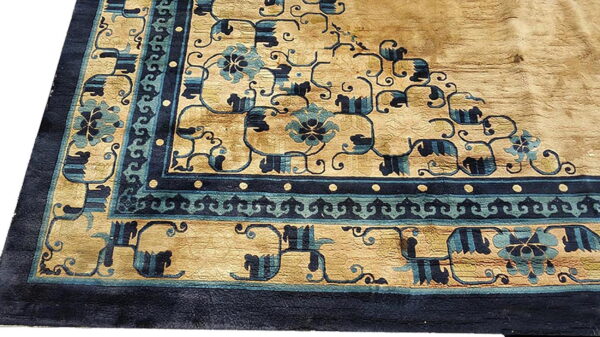 A rug corner showing a tan field and elaborate navy and teal geometric scrollwork borders.