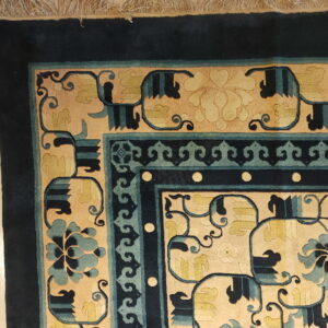 Corner view of a plush, ornate rug featuring navy, teal, and tan borders with light fringes.