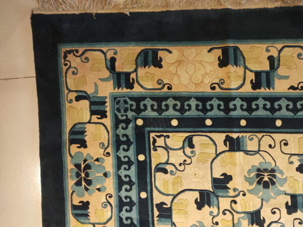 Corner view of a plush, ornate rug featuring navy, teal, and tan borders with light fringes.