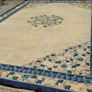 Oversized cream and gold rug with wide navy and light blue borders lays outdoors on gray concrete.