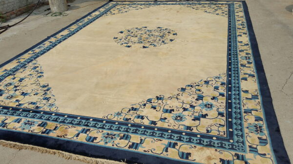 Oversized cream and gold rug with wide navy and light blue borders lays outdoors on gray concrete.
