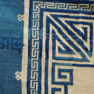 The rug features a bold blue and beige Greek key border with detailed geometric corner designs.
