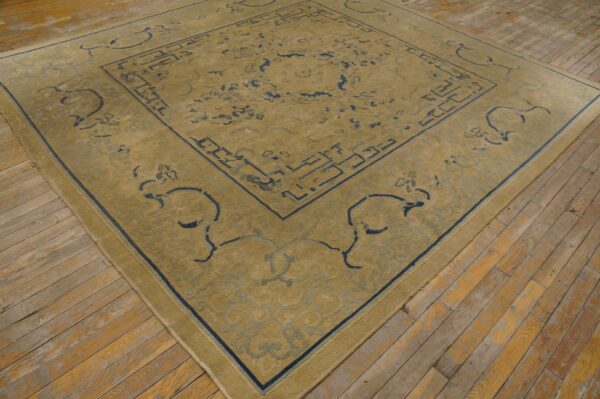 Gold and blue patterned rug with low pile rests on light brown, distressed wood flooring.
