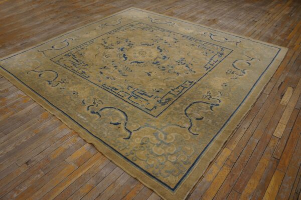 Gold rug featuring a complex blue border and central design on worn wood flooring.