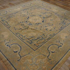 Tan rug with indigo blue geometric and curvilinear motifs displayed on rustic wide plank wood flooring.
