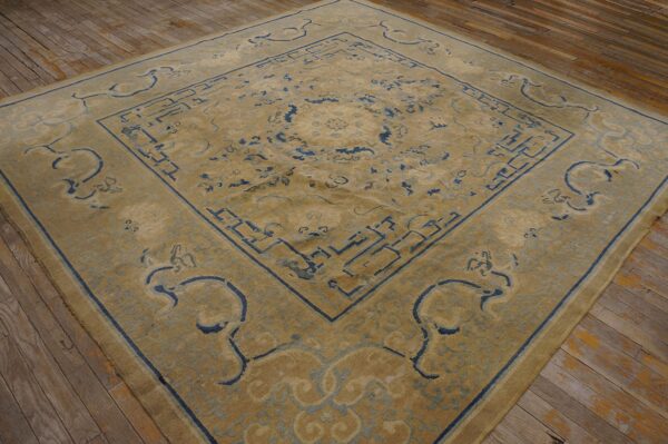 Tan rug with indigo blue geometric and curvilinear motifs displayed on rustic wide plank wood flooring.