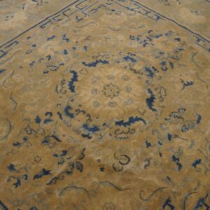 Golden tan rug with dark blue traditional floral motifs and a geometric border on wood flooring.