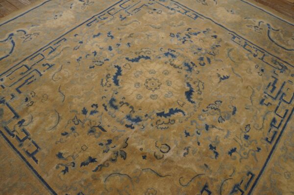 Golden tan rug with dark blue traditional floral motifs and a geometric border on wood flooring.