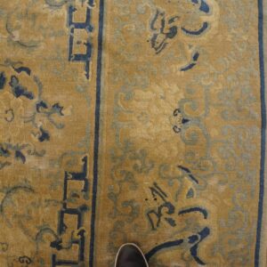 Mustard yellow rug with dark and light blue scrolling patterns and a geometric border on rustic wood.