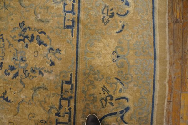 Mustard yellow rug with dark and light blue scrolling patterns and a geometric border on rustic wood.