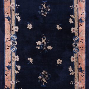 A navy blue rug with a wide peach border and traditional floral and bird motifs in beige and blue.