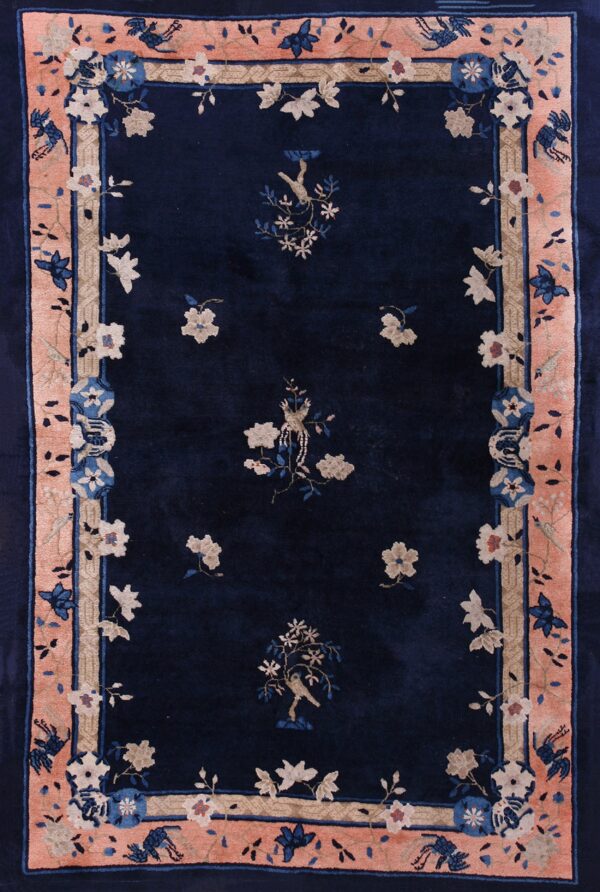 A navy blue rug with a wide peach border and traditional floral and bird motifs in beige and blue.