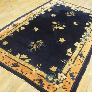 Navy blue rug with a light floral pattern and wide contrasting orange and cream border on wood flooring.
