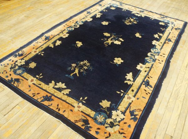 Navy blue rug with a light floral pattern and wide contrasting orange and cream border on wood flooring.