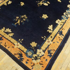 Navy blue rug with floral patterns, featuring cream and coral borders, on light wood flooring.