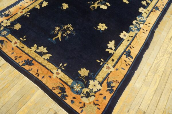 Navy blue rug with floral patterns, featuring cream and coral borders, on light wood flooring.