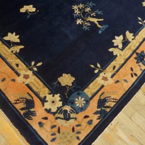 Navy blue rug with floral and bird motifs, featuring wide peach and gold patterned borders on wood flooring.