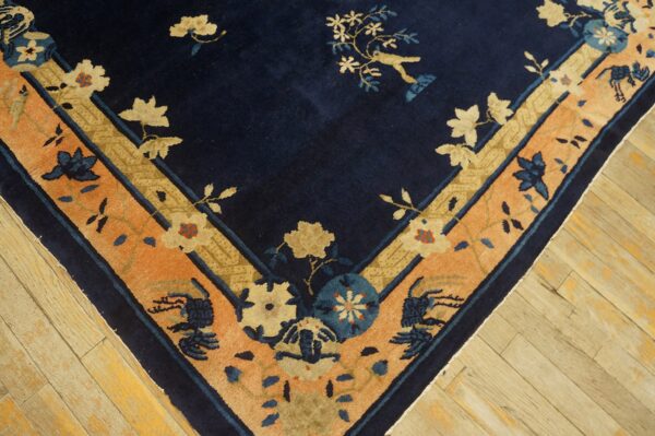 Navy blue rug with floral and bird motifs, featuring wide peach and gold patterned borders on wood flooring.