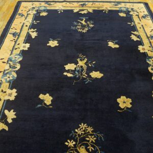 Navy blue rug with gold floral sprays and bird designs bordered by peach and gold panels on wood floors.