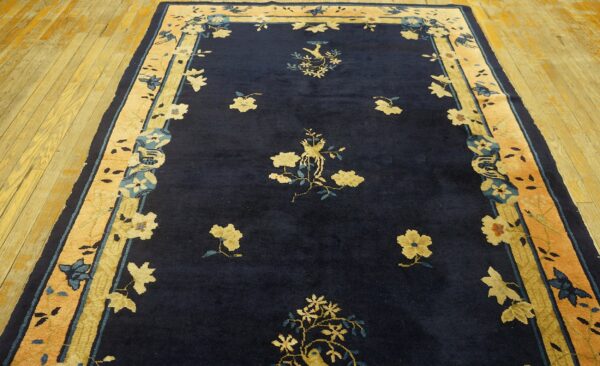 Navy blue rug with gold floral sprays and bird designs bordered by peach and gold panels on wood floors.