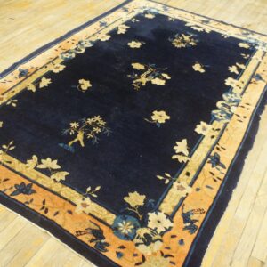 Navy blue rug with a naturalistic floral pattern and a wide peach border on pale wood floors.