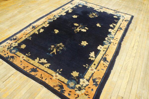 Navy blue rug with a naturalistic floral pattern and a wide peach border on pale wood floors.
