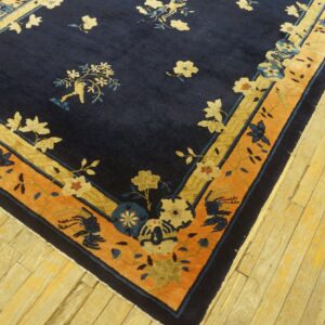 A deep blue floral rug bordered in contrasting orange and gold rests on light wood planks.