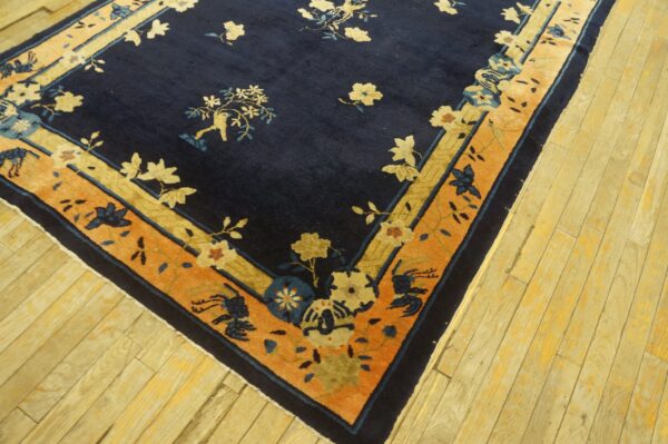 A deep blue floral rug bordered in contrasting orange and gold rests on light wood planks.